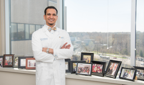 Dr. Karim Qumosani stands in his office among photos of family, team members, and patients.