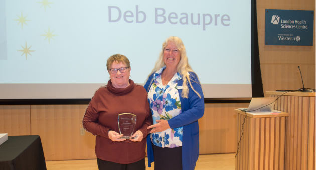 Two people stand one holding award