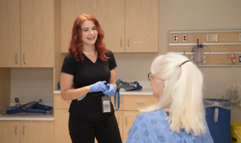 A health-care professional with red hair speaks to a patient in a medical examination room.