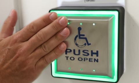 A photo of a hand touching a button to open a wheelchair accessible door.