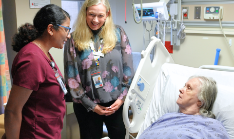 Patient in bed speaks with nurse and improvement specialist about patient safety.