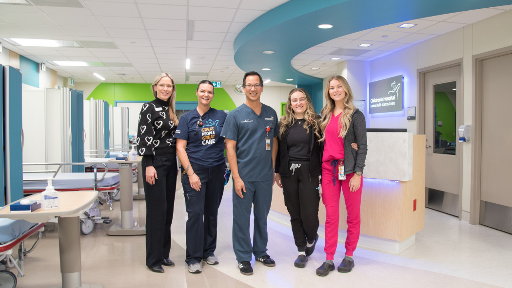 Five medical professionals stand together in a hospital hallway, smiling at the camera.